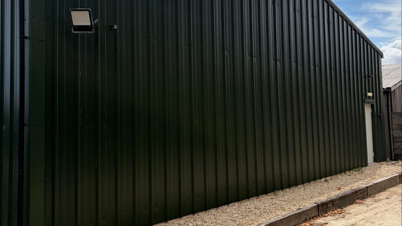 Exterior wall of a dark green storage building fitted with security lighting