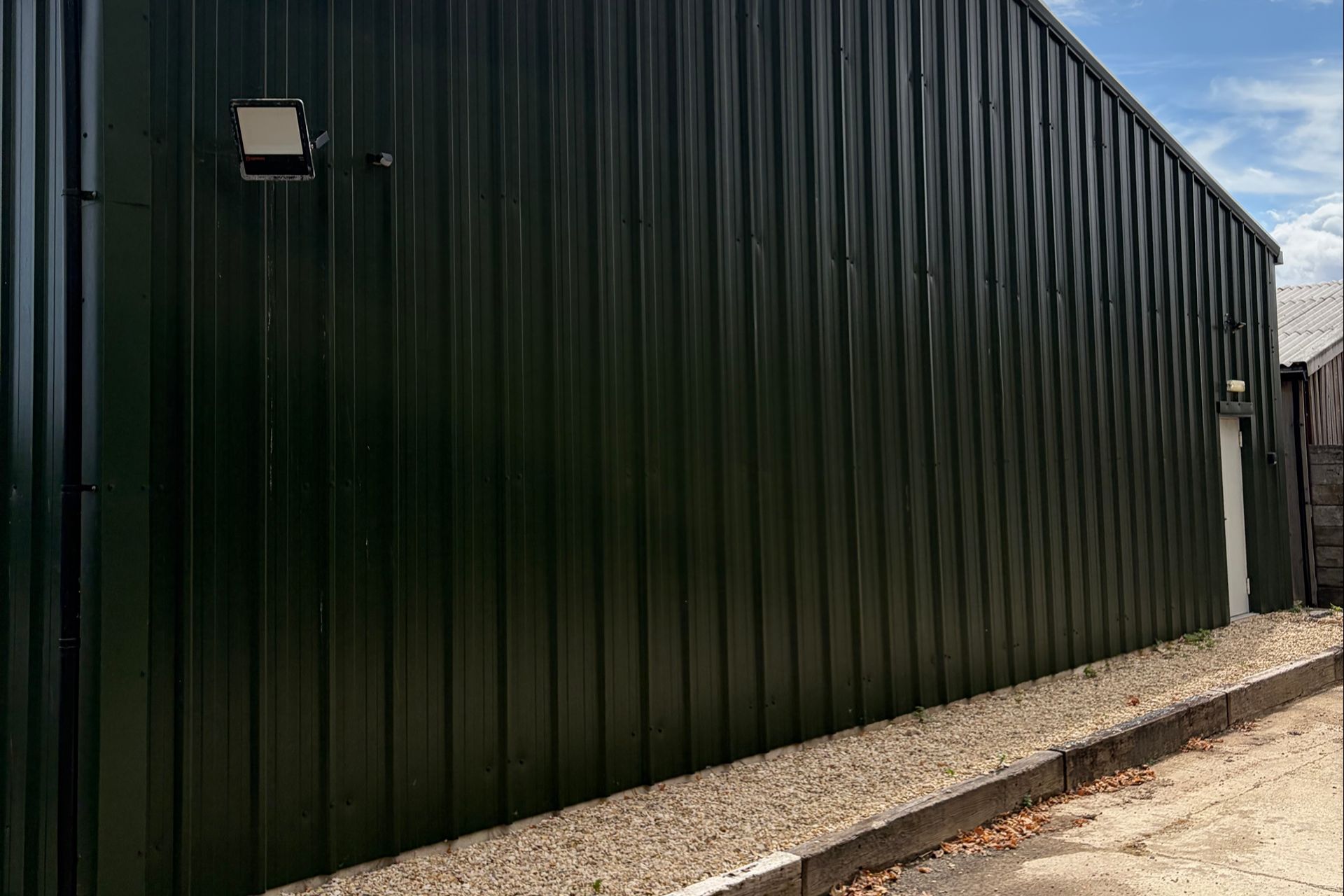 Exterior wall of a dark green storage building fitted with security lighting